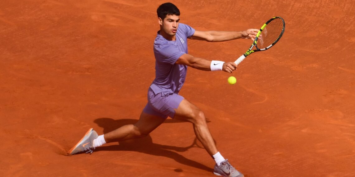 Jogador de tênis em quadra de saibro, concentrado, rebatendo bola com raquete em movimento de backhand.