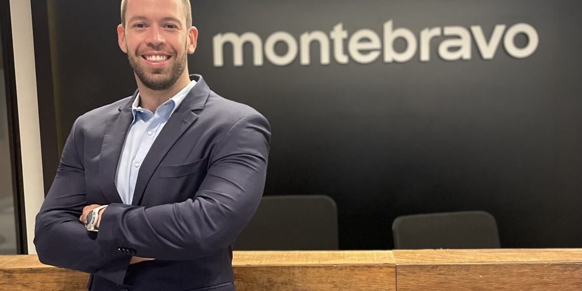 Homem sorridente de terno azul-escuro, braços cruzados, em frente ao logo da empresa Monte Bravo em um escritório moderno.