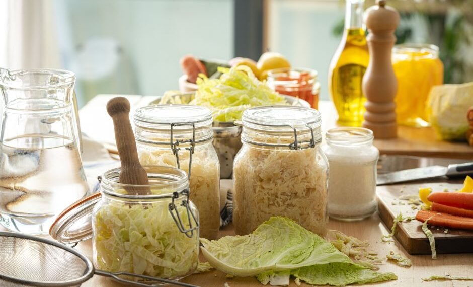 Preparação de alimentos fermentados em potes de vidro, com repolho, cenouras, temperos e óleo sobre a mesa de cozinha.