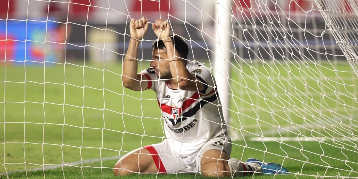 Jogador frustrado dentro do gol, segurando a rede, após lance no estádio. Futebol, emoção, competição.
