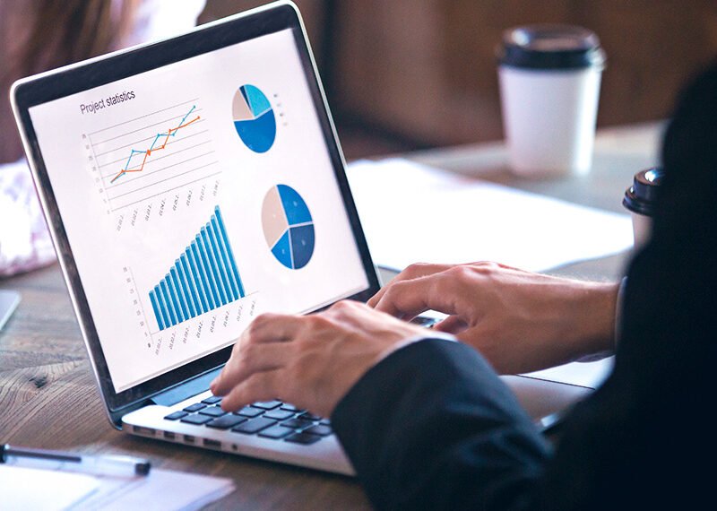 Pessoa analisando gráficos e estatísticas de projeto em laptop, com foco em dados de crescimento, produtividade e tomadas de decisão.