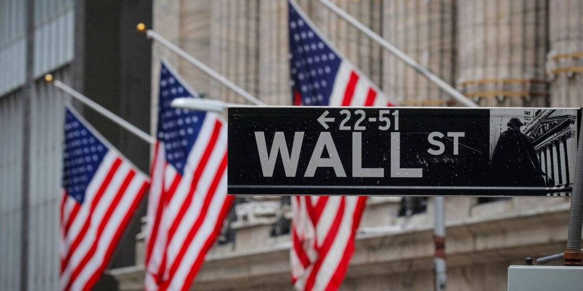 Placa de Wall Street com bandeiras americanas ao fundo, representando o centro financeiro dos Estados Unidos.