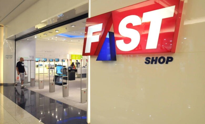 A imagem mostra a entrada de uma loja chamada Fast Shop, com um grande letreiro em destaque. O letreiro é composto pelas palavras