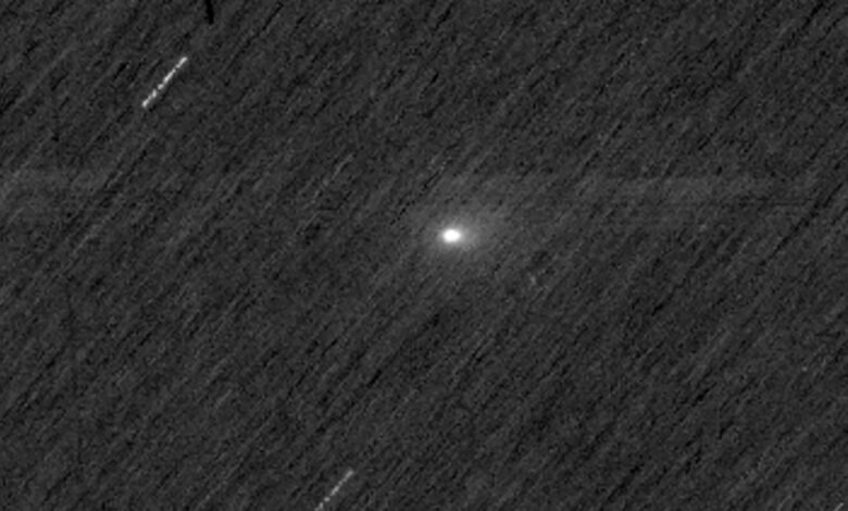 Cometa com núcleo brilhante e cauda difusa visível no centro da imagem, sobre fundo escuro pontilhado por estrelas desfocadas e traços de movimento.