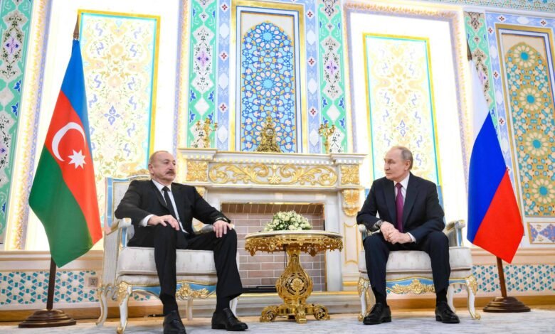 Presidente do Azerbaijão e presidente da Rússia sentados em cadeiras elegantes em sala decorada com padrões geométricos e florais. Bandeiras do Azerbaijão e da Rússia posicionadas ao lado de cada líder, com mesa dourada e arranjo floral entre eles.