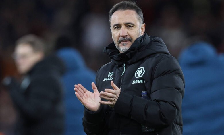 Treinador Vítor Pereira com casaco preto acolchoado com logotipo do Wolverhampton Wanderers aplaude em campo. Fundo desfocado mostra outras pessoas e ambiente de estádio à noite.