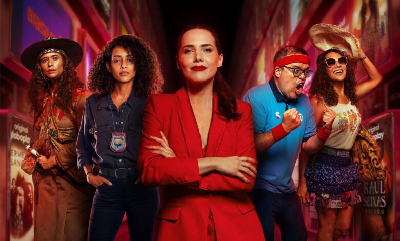 Cinco pessoas em pé em uma rua iluminada à noite. No centro, mulher de terno vermelho com braços cruzados. Ao redor, pessoas com roupas casuais e estilos variados. Texto