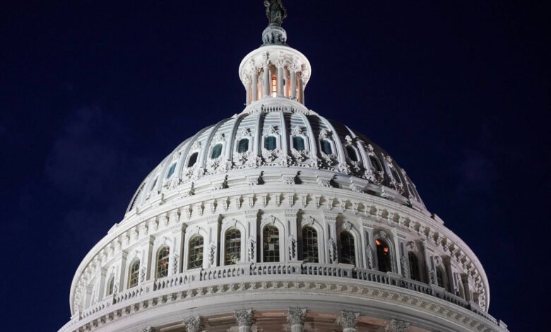 Vista frontal da cúpula branca do Capitólio dos Estados Unidos iluminada contra o céu noturno escuro. Detalhes arquitetônicos e janelas são visíveis.
