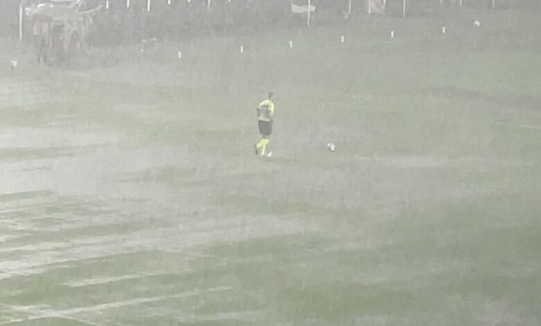 Chuva interrompe partida de futebol entre Vasco e Internacional no estádio São Januário, com campo encharcado e jogadores aguardando retomada do jogo.