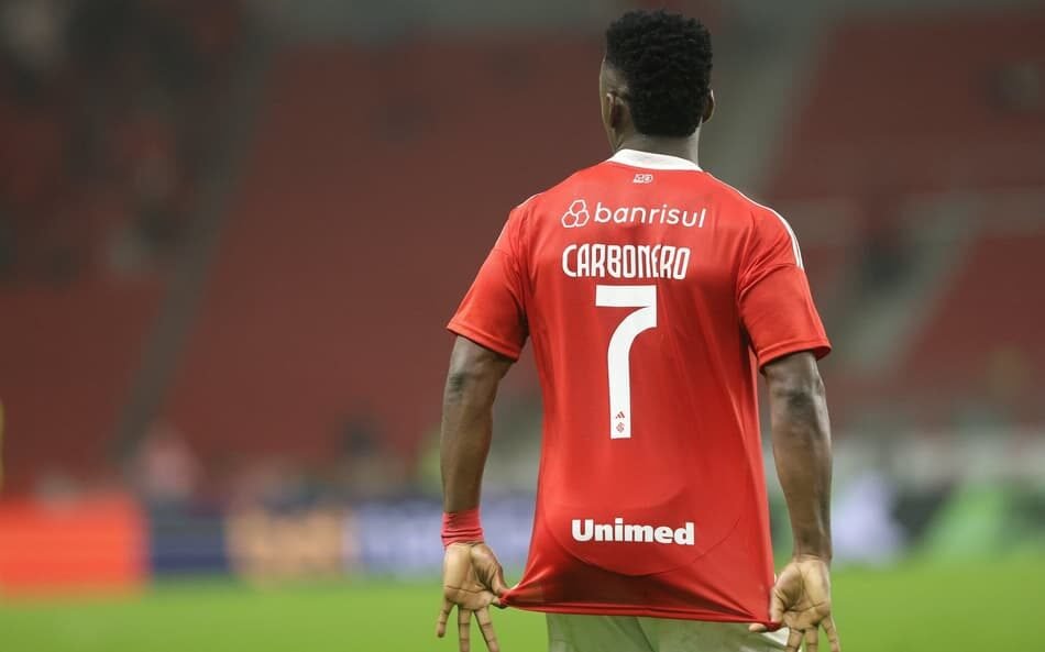 Fotografia de Johan Carbonero com a camisa do Internacional, após ser adquirido pelo clube em uma transação milionária, destacando seu entusiasmo em um estádio de futebol.